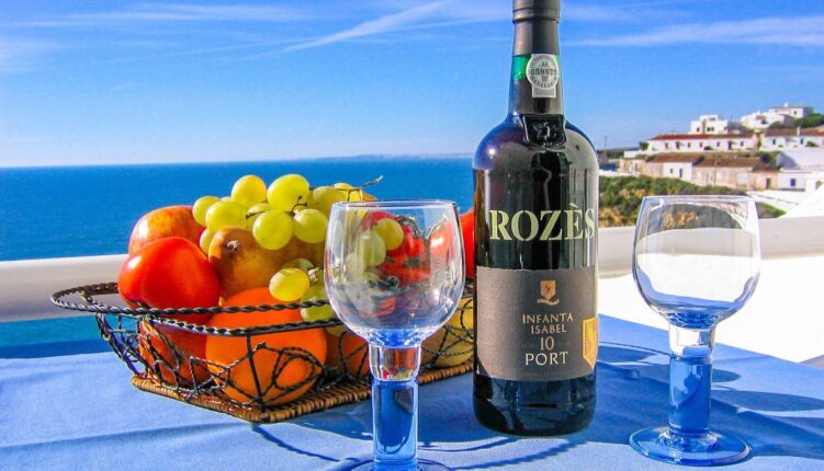 bottle of port with glasses and bowl of fruit on a table overlooking Carvoeiro bay