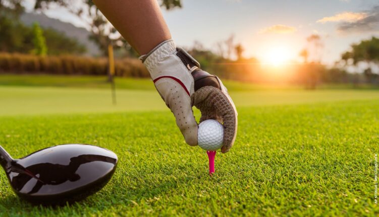 gloved hand placing a golf ball on a tee at sunset