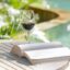 Glass of red wine on a table with an open book by a swimming pool