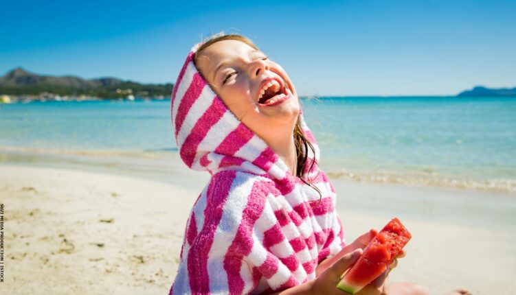 Child laughing on a beach holding water melon