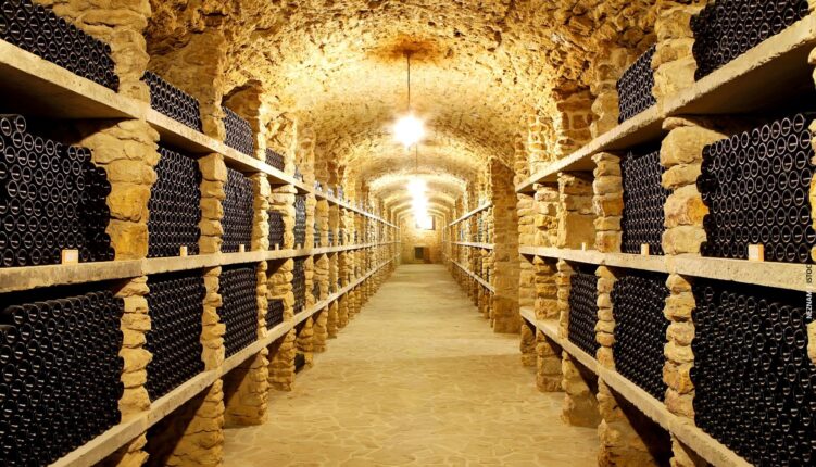 Lit wine cellar with bottles neatly stacked and rock walls and ceiling