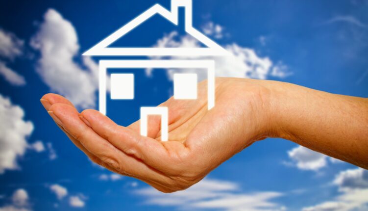 Hand holding outline of house with blue sky and clouds in the background